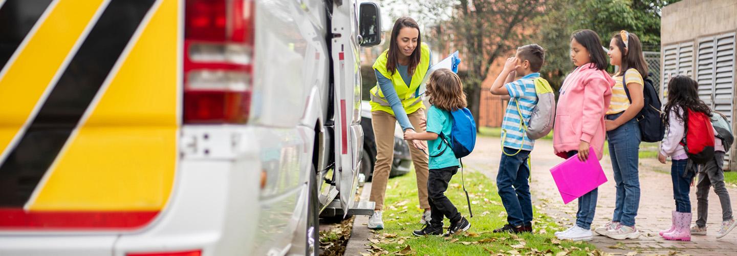 a teacher helps students board the school bus