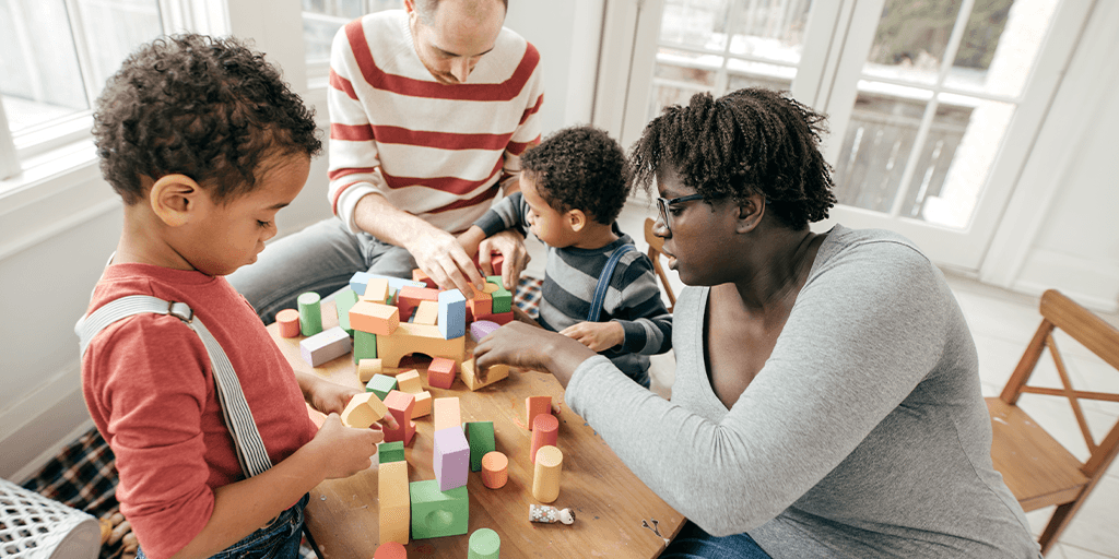 Two adults and young children play with building blocks