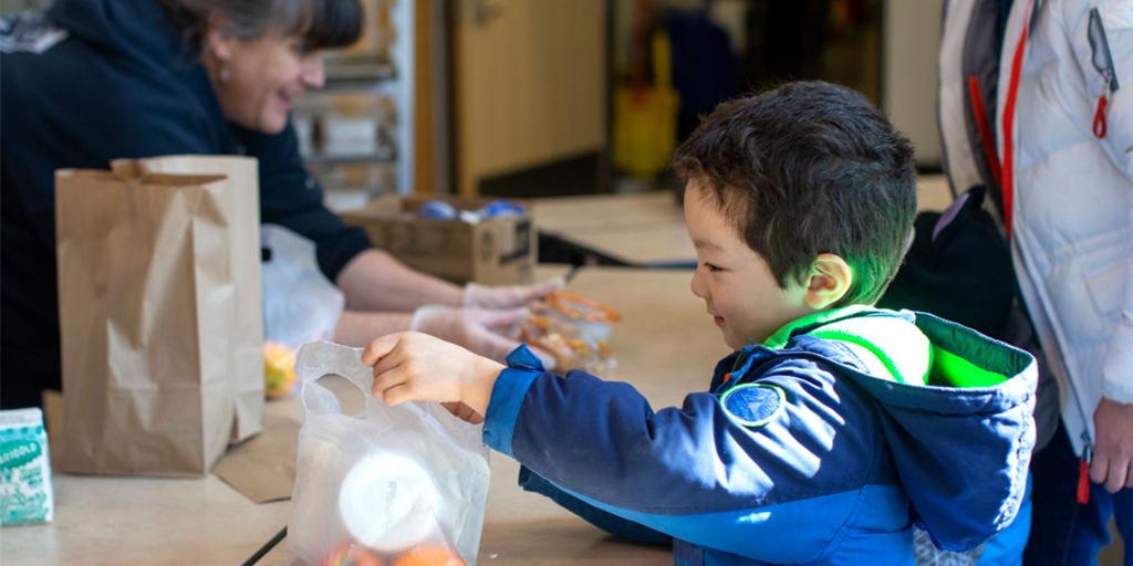 a young boy picks up a bag of food