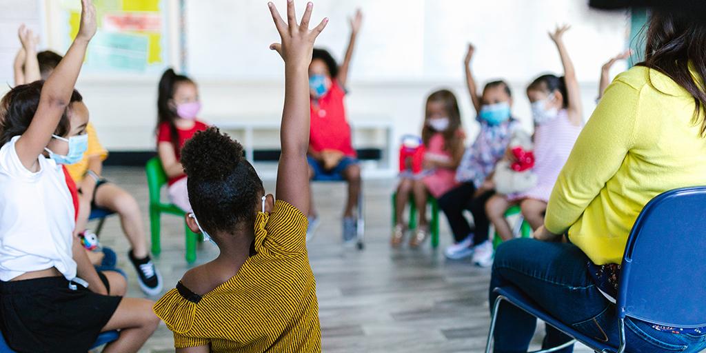 a group of children raise their hands in class