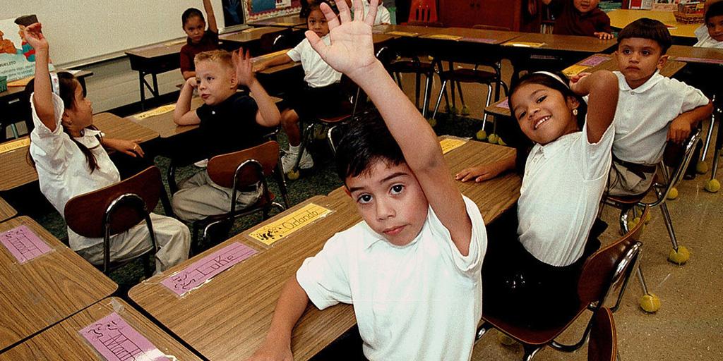 young children raising their hands in a classroom